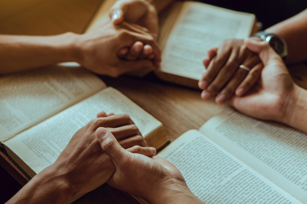 Clasped hands over open Bibles.
