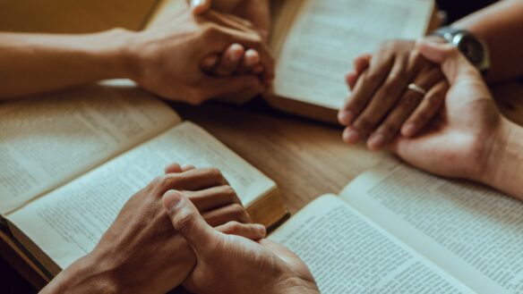 Clasped hands over open Bibles.